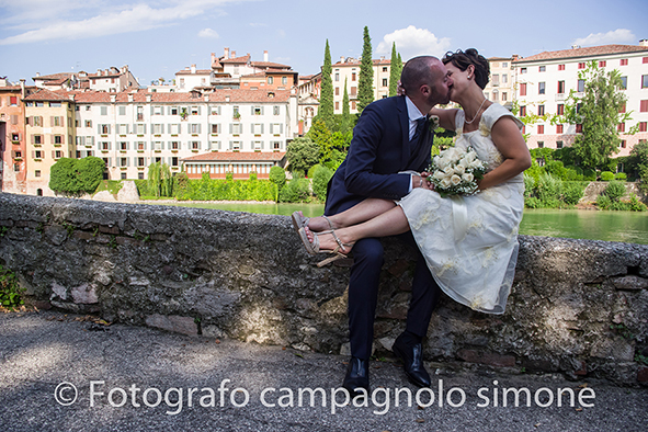 Fotografo matrimoni Rosà, fotografia matrimonio Bassano del grappa, servizio fotografico matrimoniale a Rosà e Bassano del Grappa,, fotografo sposi Rosà e Bassano del grappa, la sposa si siede e si lascia abbracciare dal suo marito seduti nel muretto vicino al ponte degli alpini