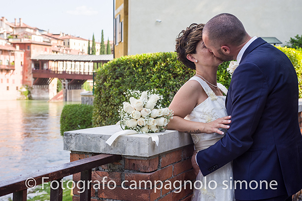 Fotografo matrimoni Rosà, fotografia matrimonio Bassano del grappa, servizio fotografico matrimoniale a Rosà e Bassano del Grappa,, fotografo sposi Rosà e Bassano del grappa, la sposa abbraccia e bacia il suo sposo, il bouquet di fiori è sopra al muretto